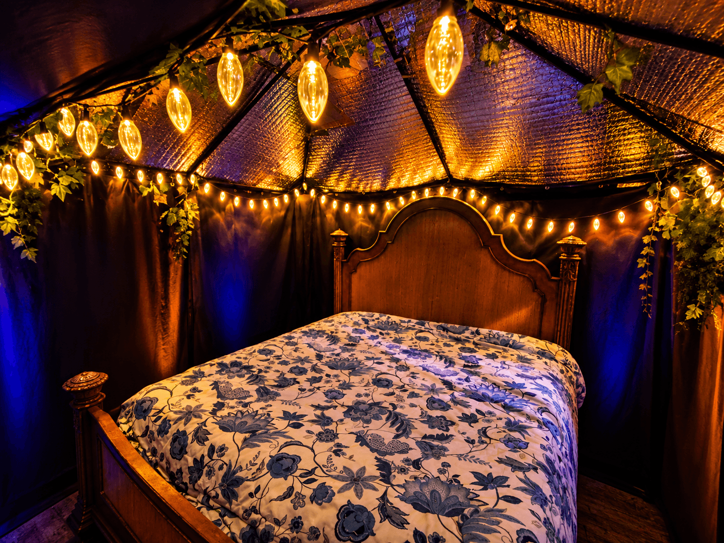 Warmly lit private play space with a bed, string lights, and dark draped walls